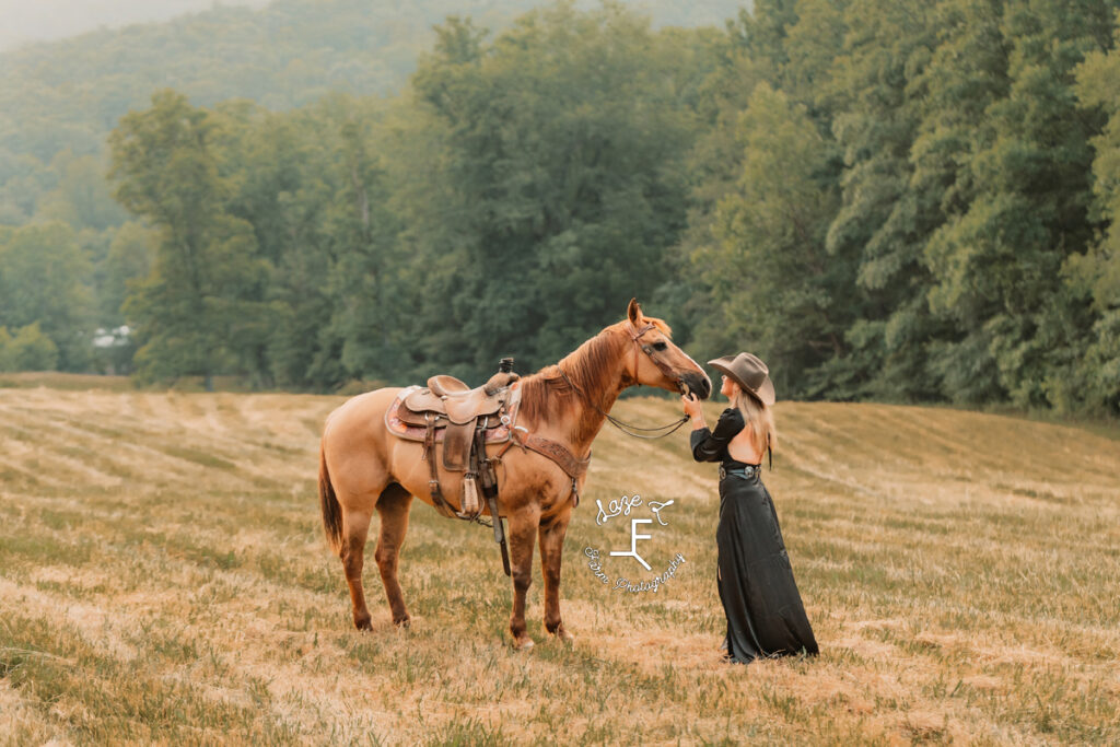 cowgirl in black dress kissing dunn horse on ground