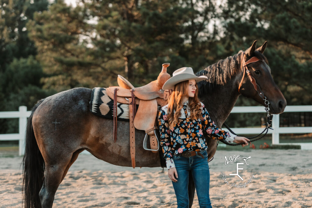 cowgirl standing at shoulder of horse looking right