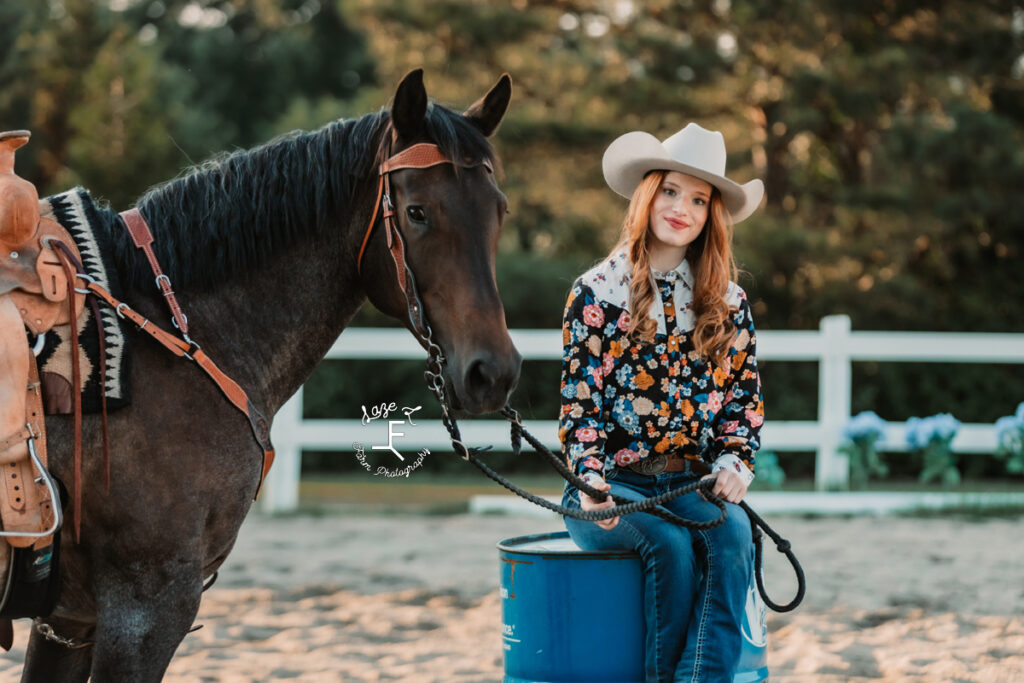 cowgirl sitting on barrel with bay roan horse