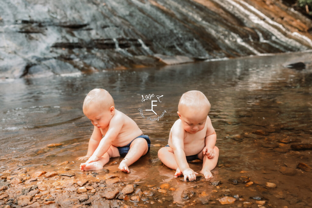 twin boys sitting in the water playing with rocks