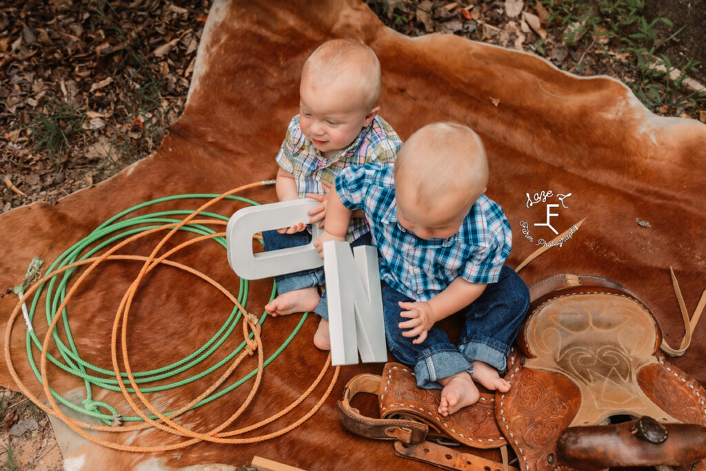 twin boys holding an o and an n on a cowhide rug with ropes and saddle