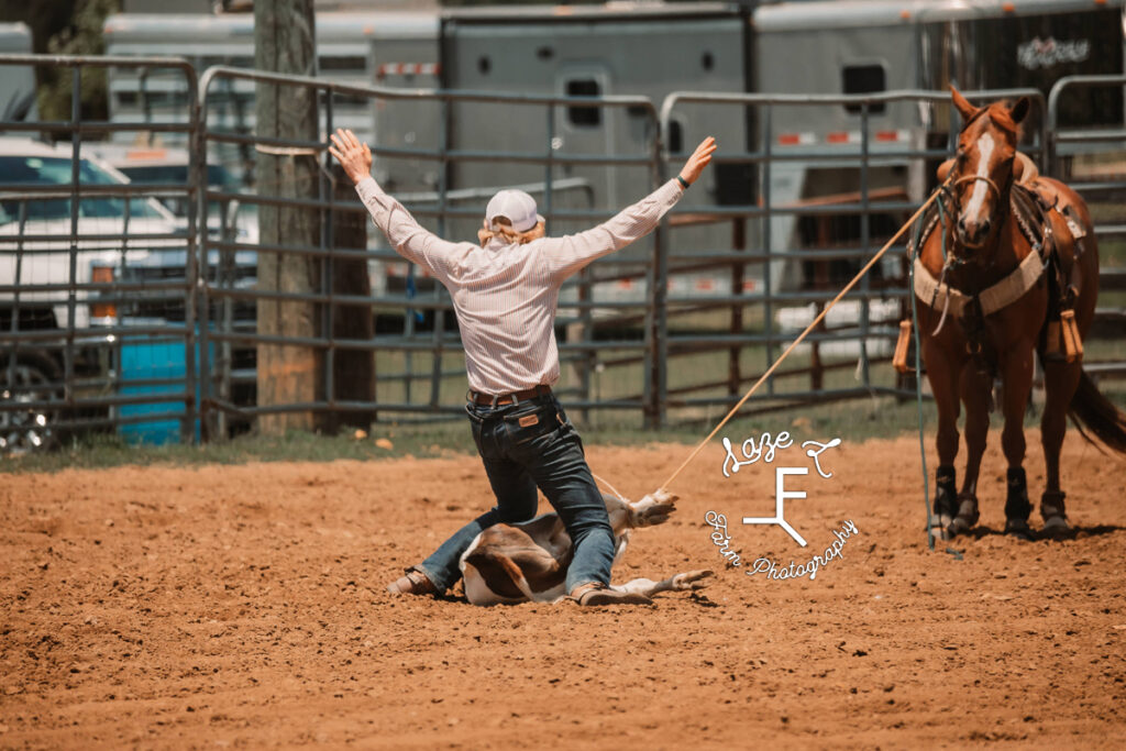 cowboy standing up from calf tying with arms in air