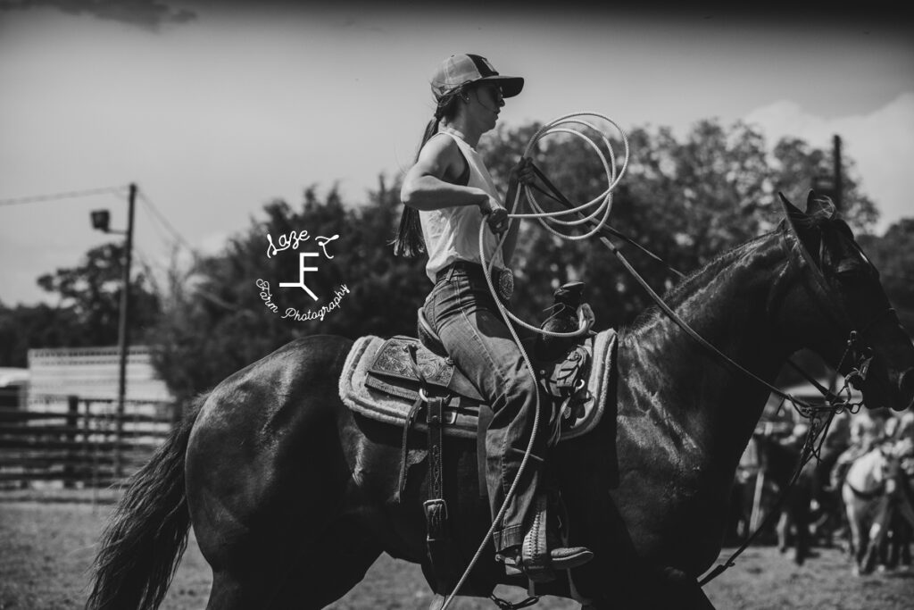 cowgirl in a trucker hat on her horse with rope in black and white
