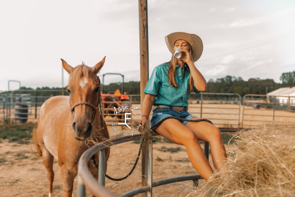 cowgirl sitting on hay ring drinking a beer with her horse