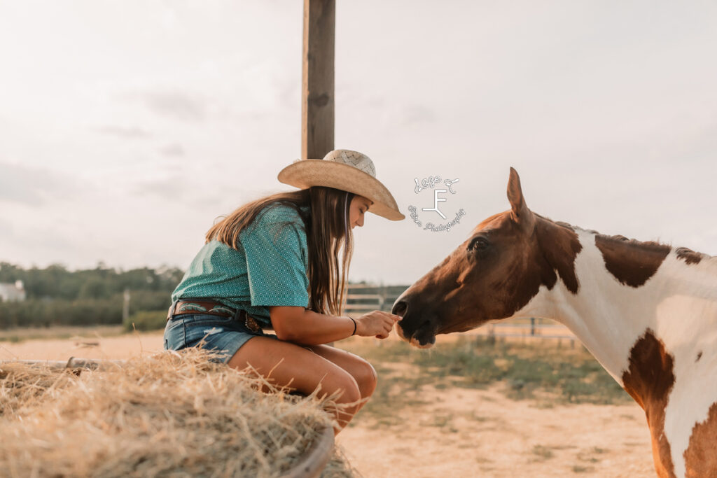 cowgirl sitting on hay ring with paint horse