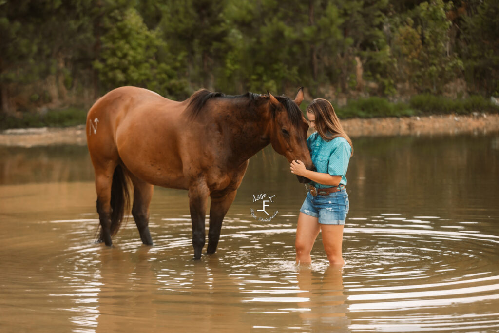 cowgirl standing in pond with bay horse