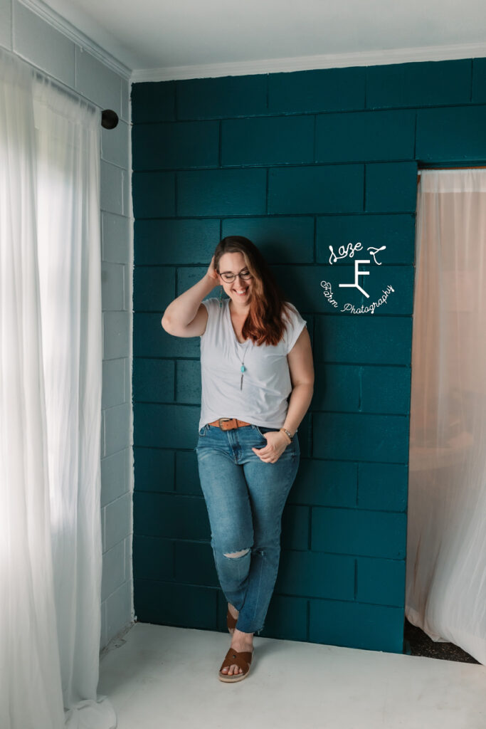 woman leaning against dark teal wall playing with hair