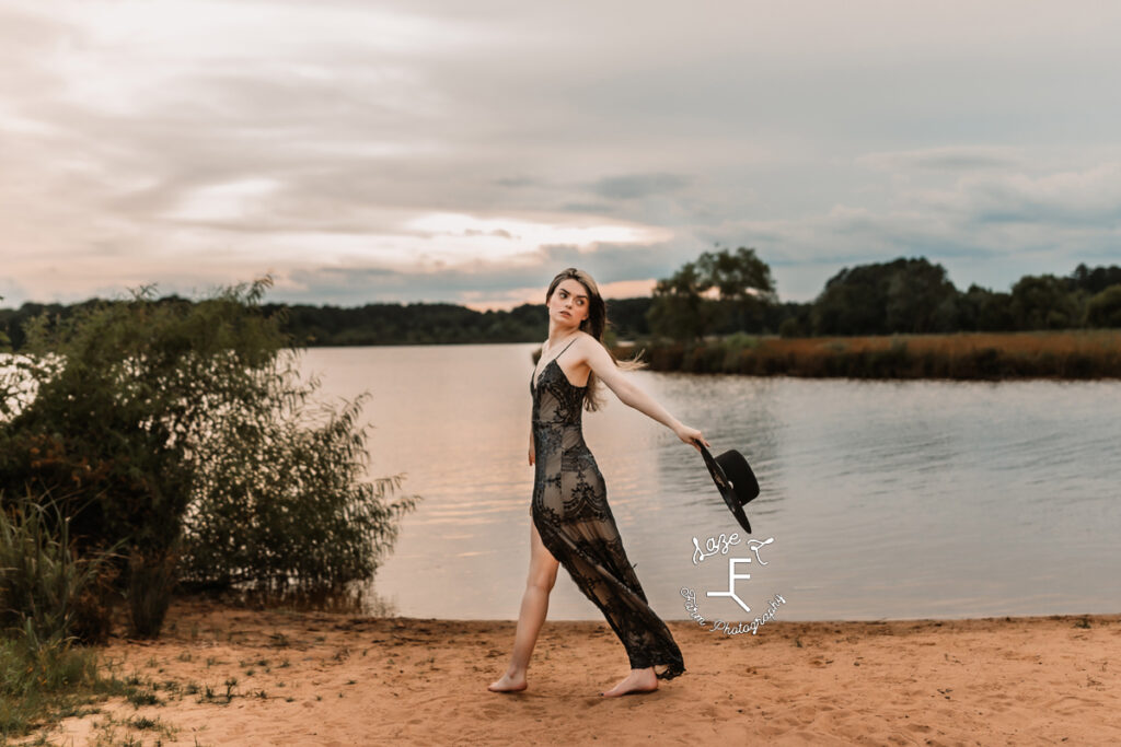 model in black lace dress holding hat walking at lake