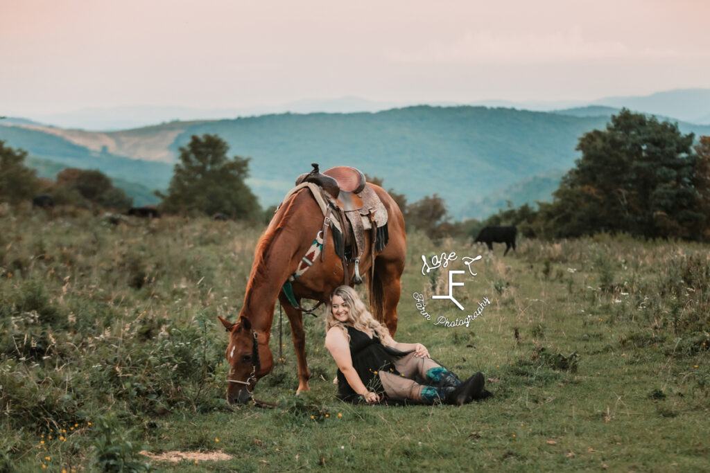 girl sitting at horses leg in black dress in front of a mountain