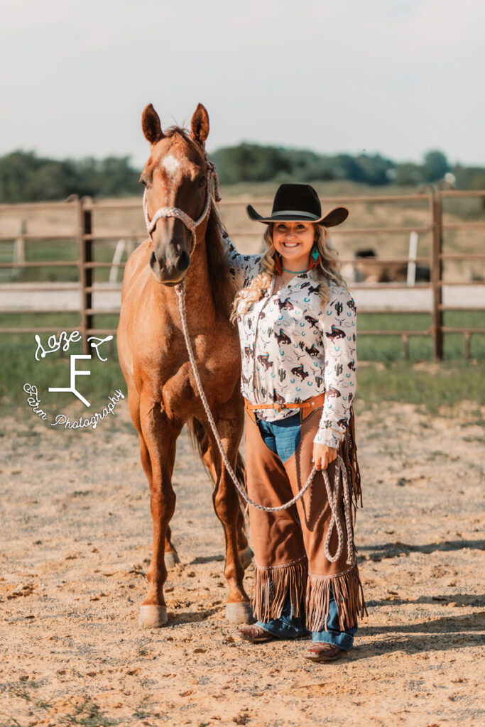 cowgirl in chaps standing beside horse