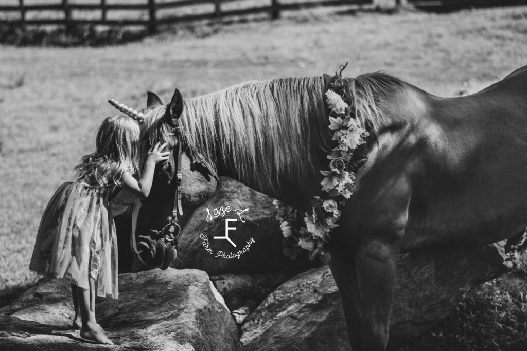 little girl kissing horse dressed like a unicorn in black and white