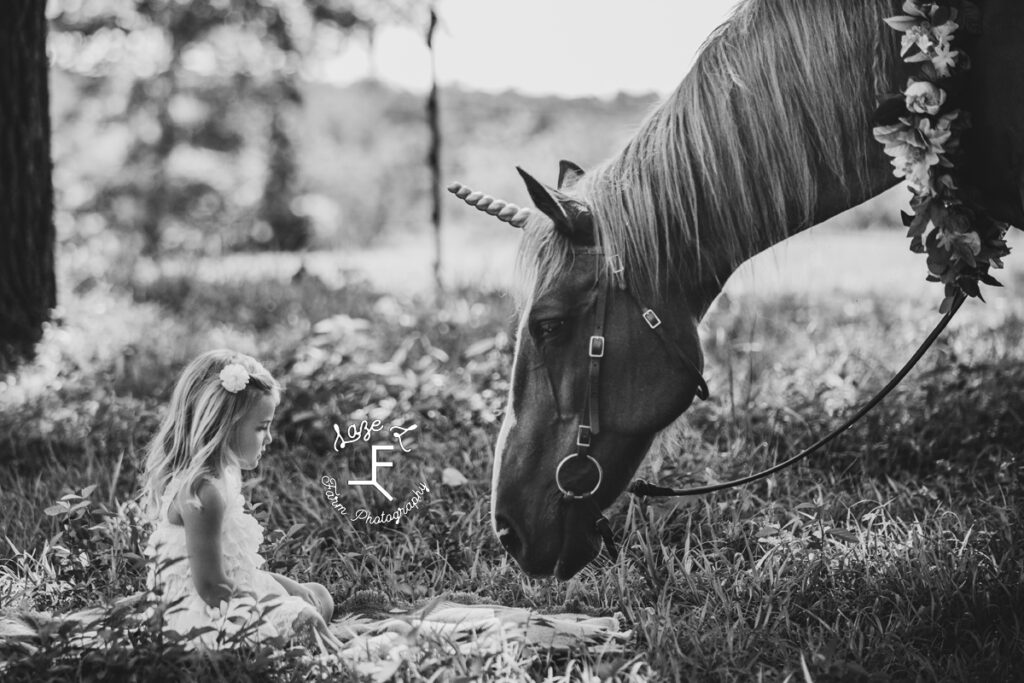 little girl sitting with unicorn horse in black and white