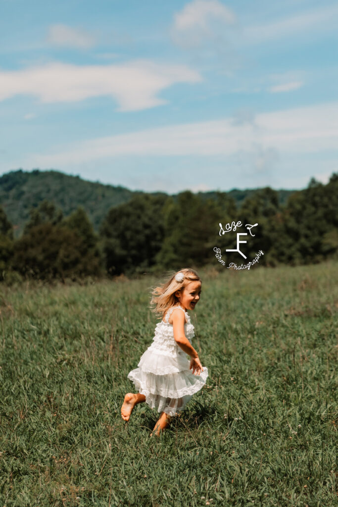 little girl running in field with mountain in background