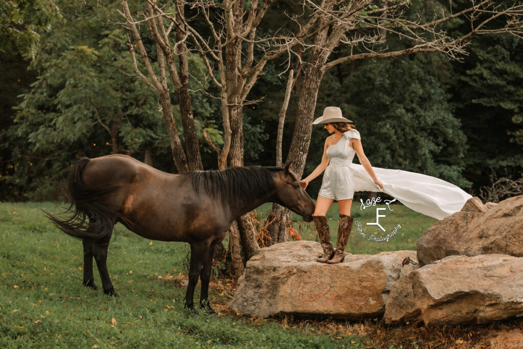 cowgirl bride standing on a rock with horse on ground beside her