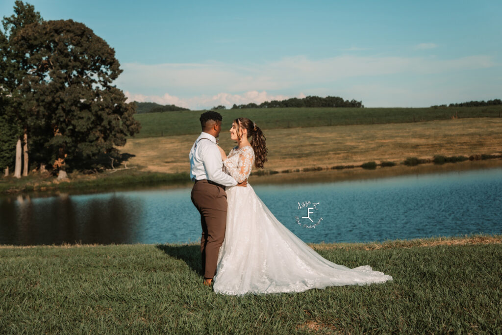 bride and groom standing facing each other with pond in background