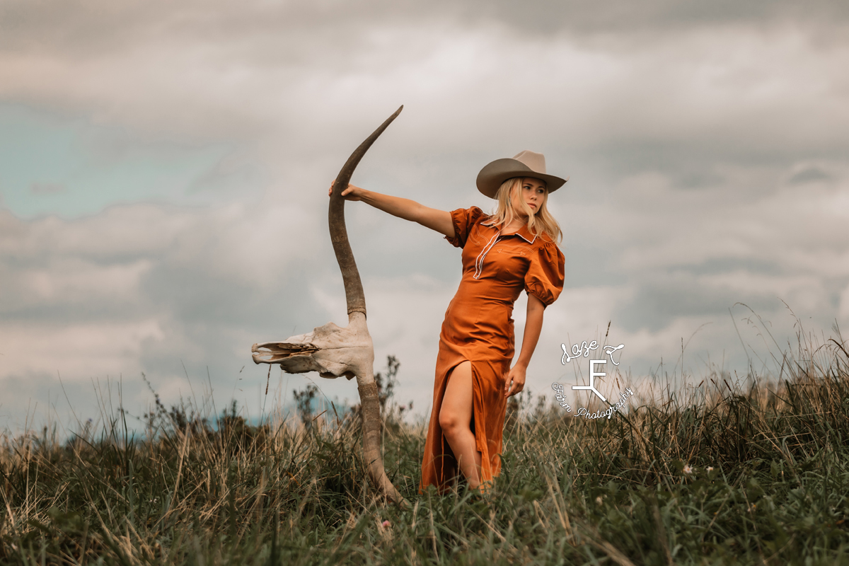 cowgirl in burnt orange dress leaning away from long horn skull