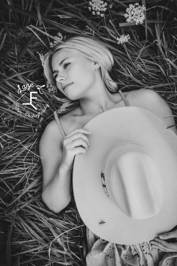 model laying in grass holding cowboy hat in black and white