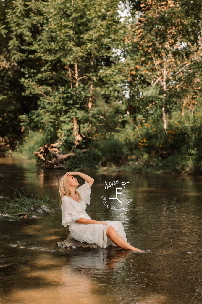 model in white dress sitting on rock in creek