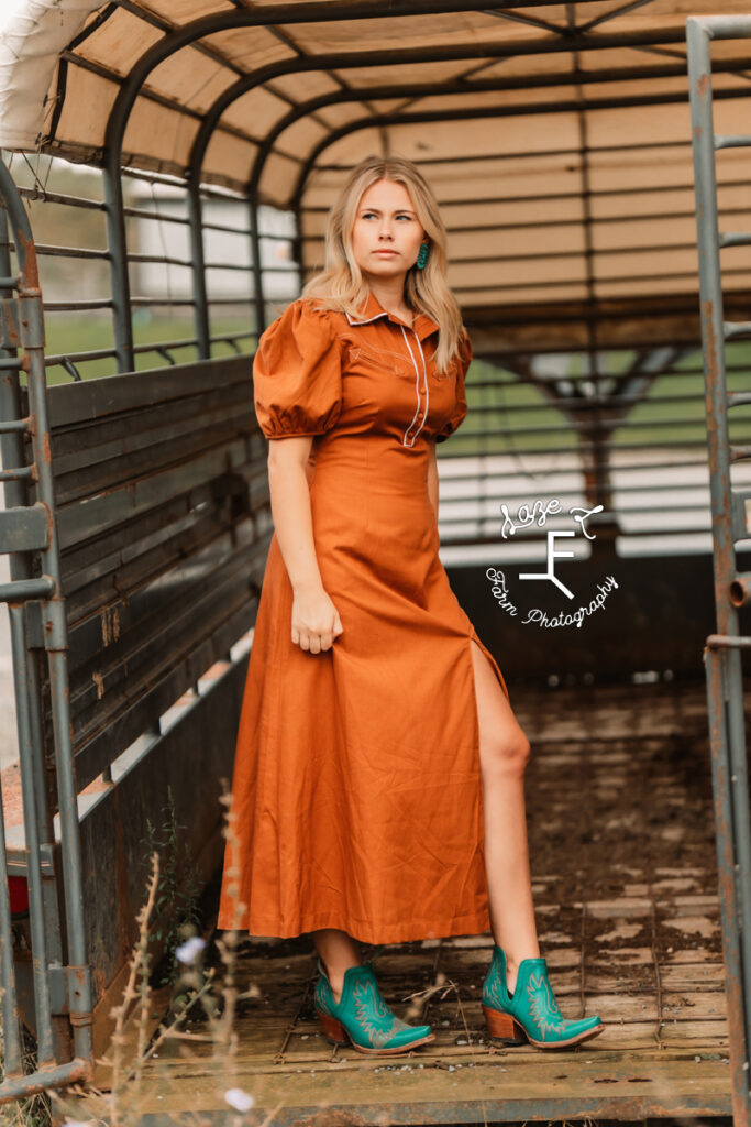 model in burnt orange dress with teal booties in stock trailer