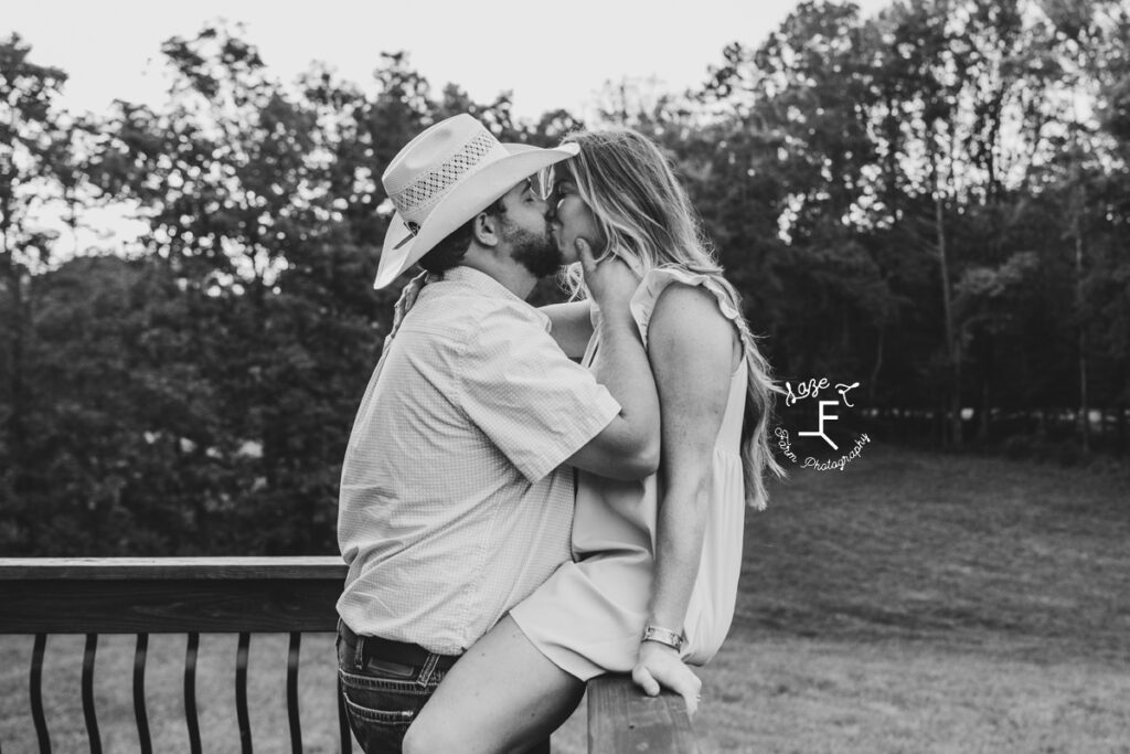 husband and wife kissing at porch rail in black and white
