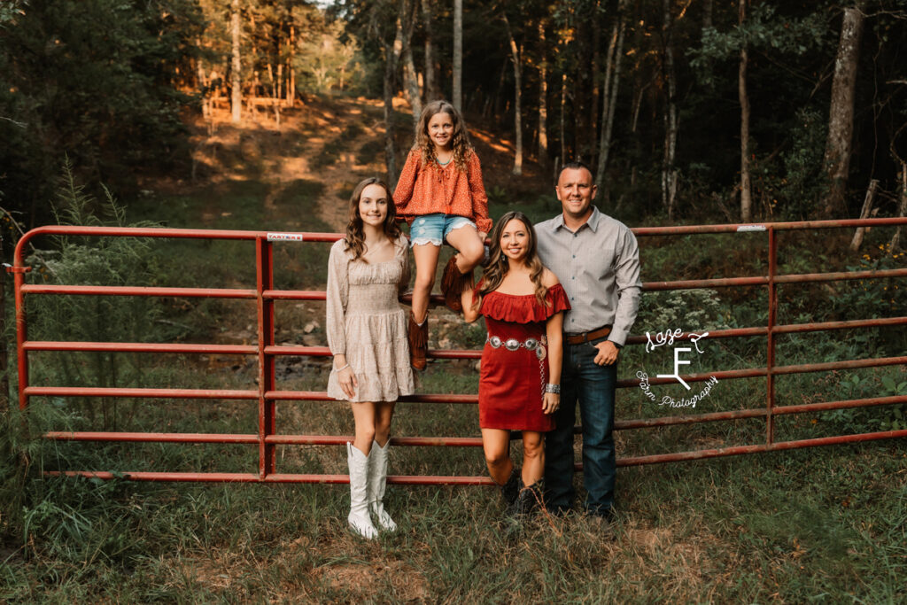 western family sitting on red gate with sun behind them