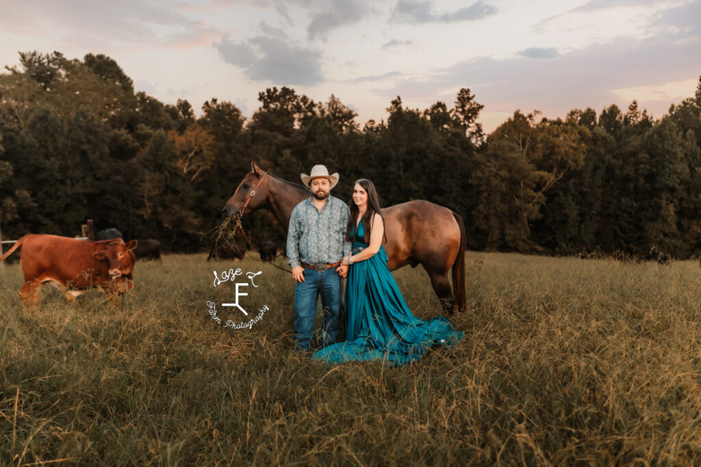 cowboy and fiancé standing with horse at sunset