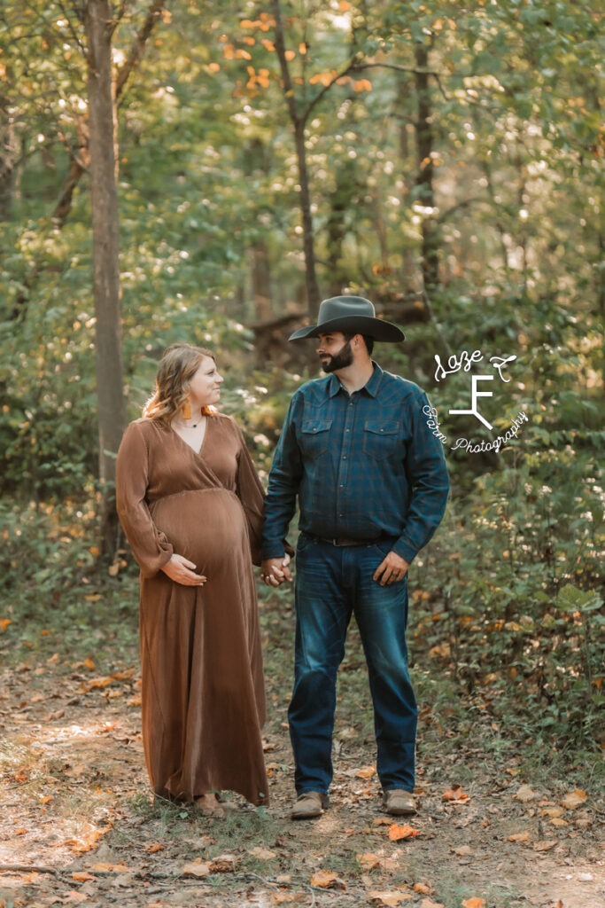 husband and pregnant wife standing in woods looking at each other