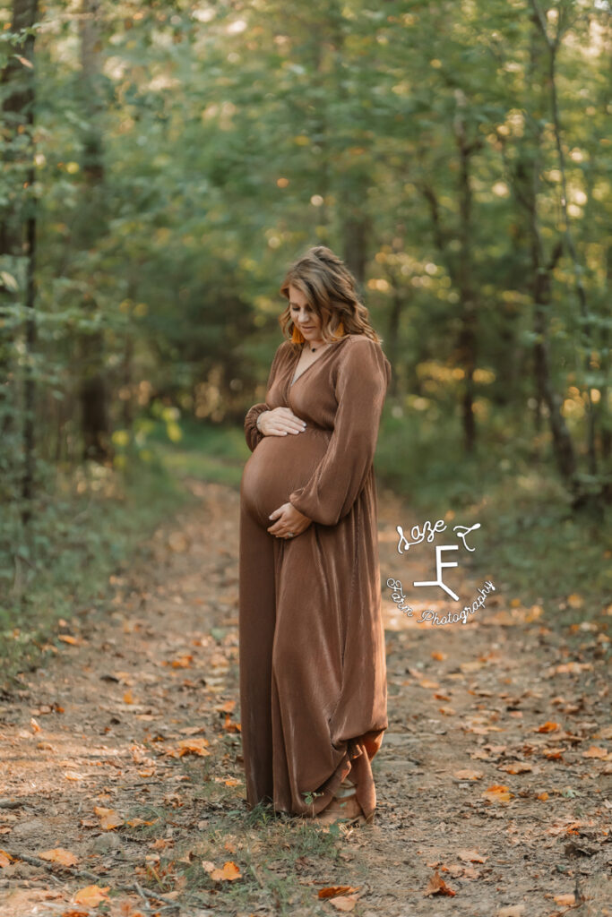pregnant woman standing in the woods on a path holding belly