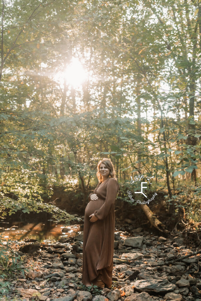 pregnant woman standing with sun coming through trees