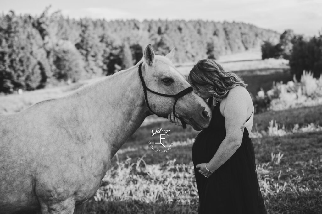 pregnant cowgirl kissing her horse on the nose in black and white