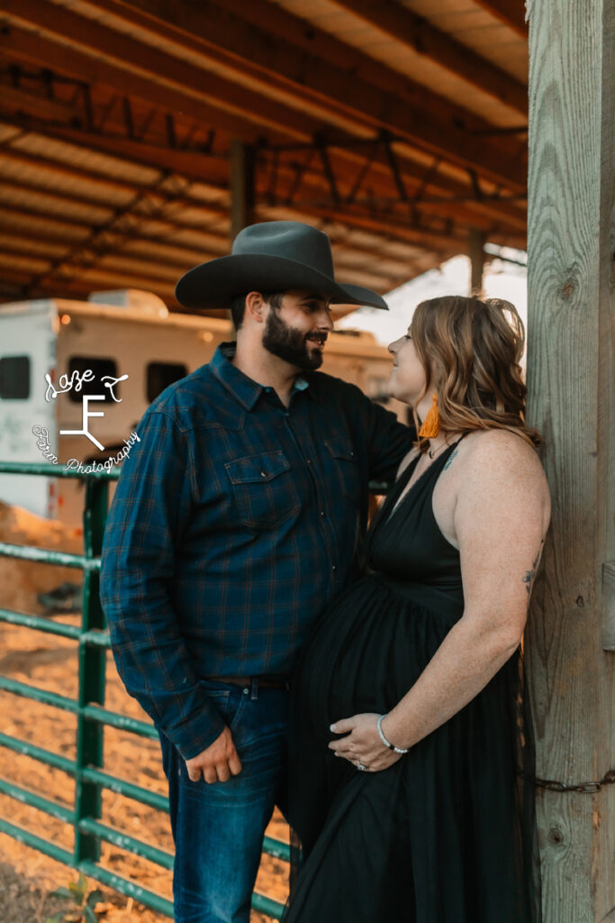 cowboy and pregnant wife leaned against post at barn