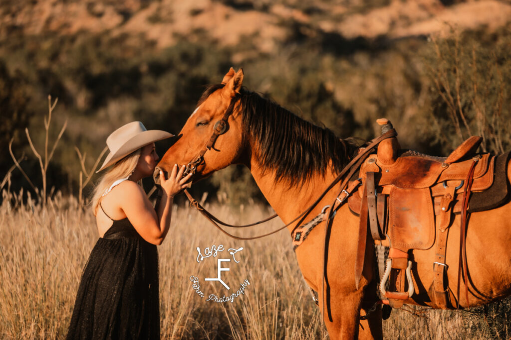 blond cowgirl in black dress kissing buckskin horse