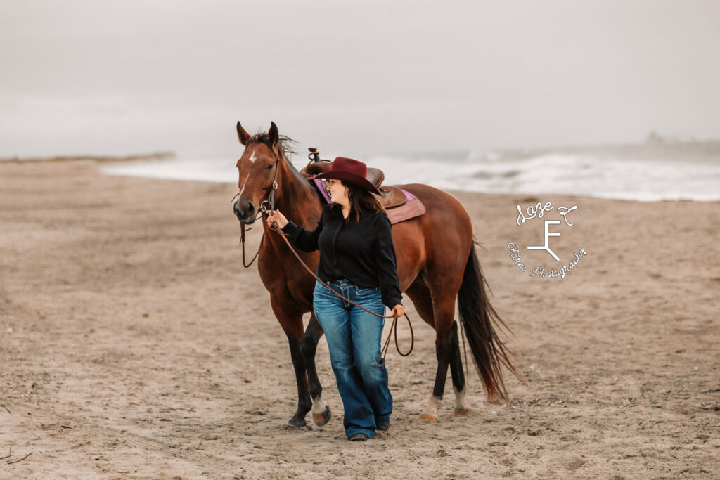 cowgirl standing with horse on the beach