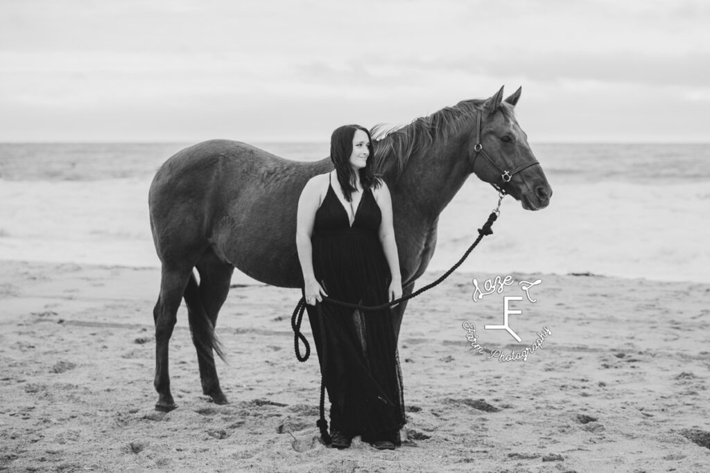 cowgirl in black dress on the beach with horse in black and white