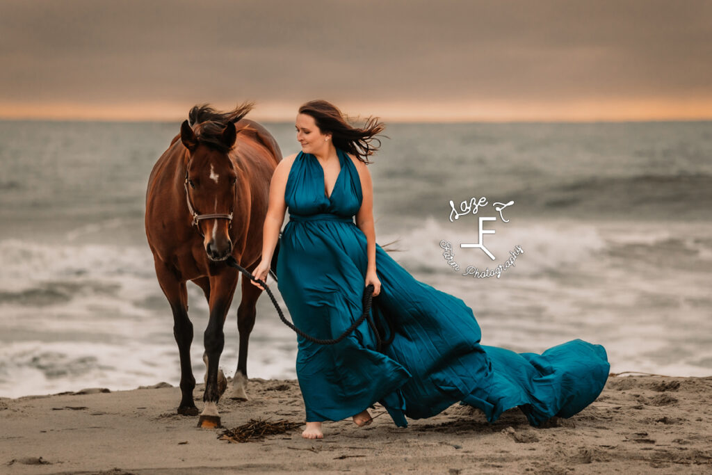 cowgirl in blue dress with horse walking from the ocean