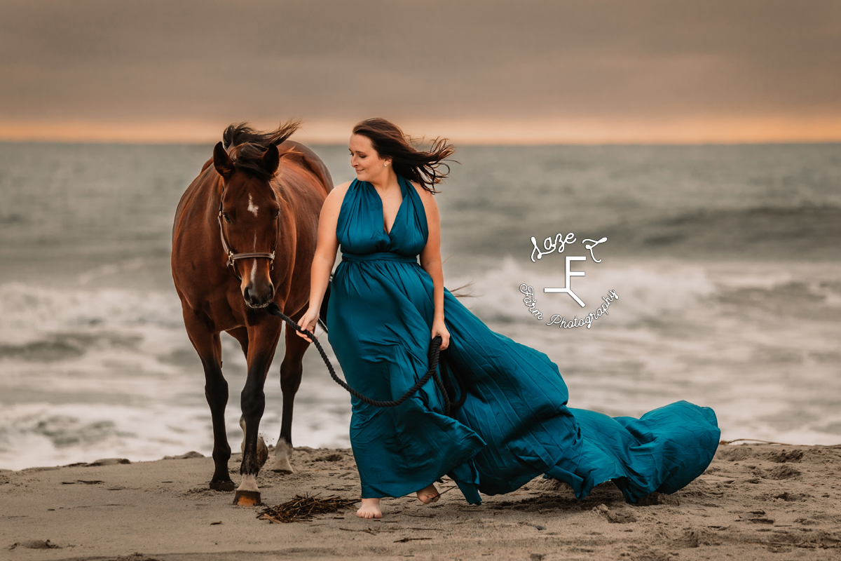 cowgirl in blue dress with horse walking from the ocean