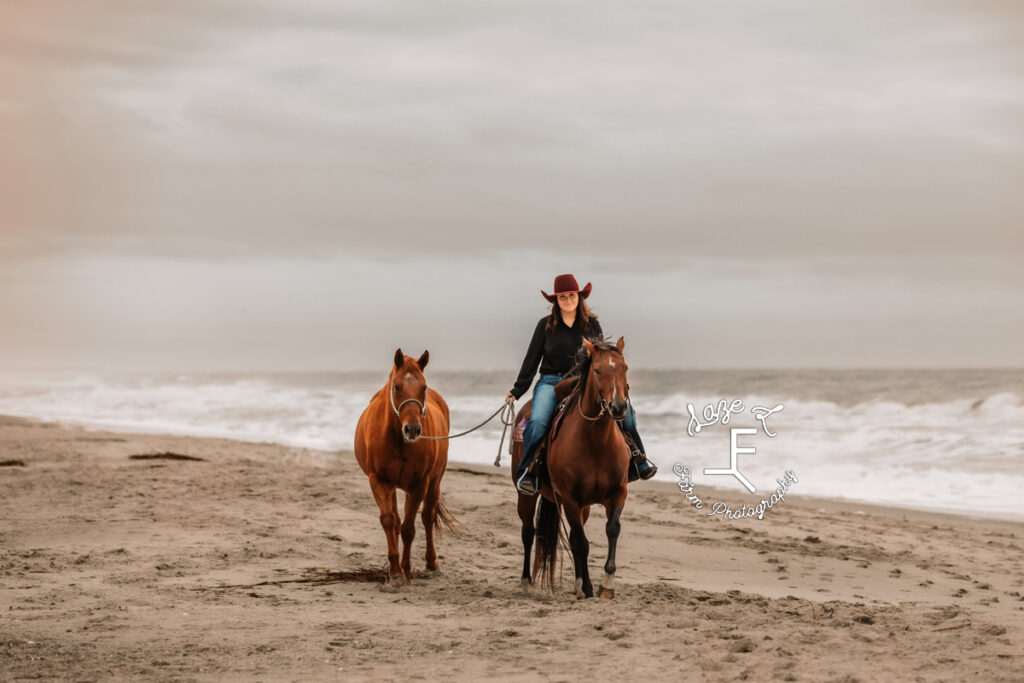 cowgirl riding one horse and ponying other down the bach