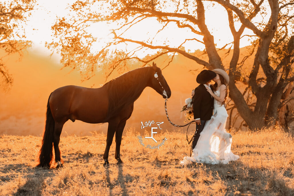 western bride and groom kissing at sunset while horse stands behind them