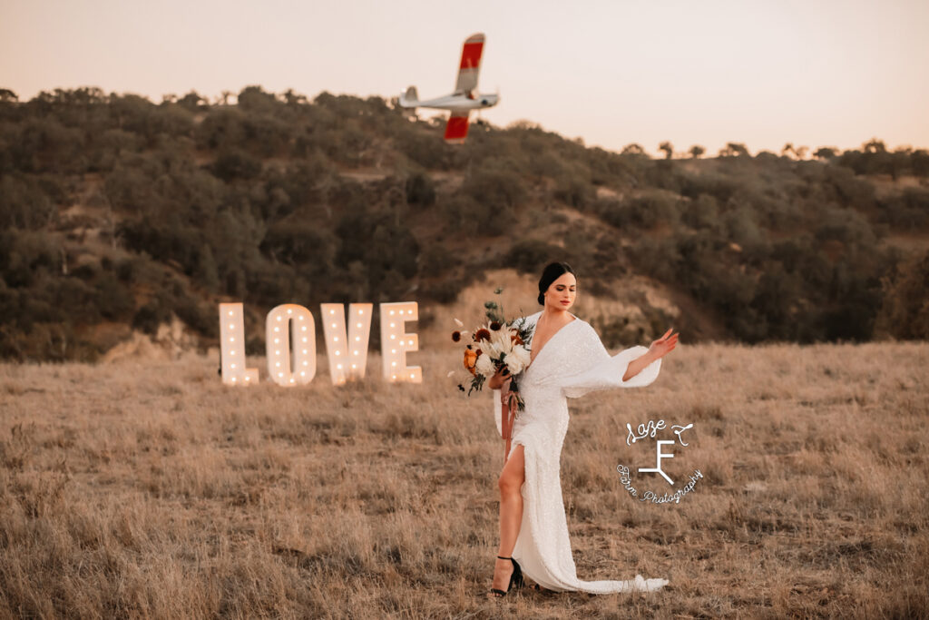 Bride model in front of giant light up love sign with a plane flying overhead