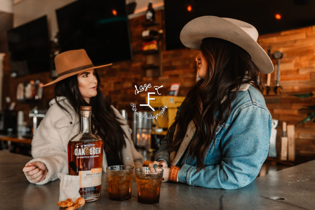 2 cowgirls talking with whiskey in foreground