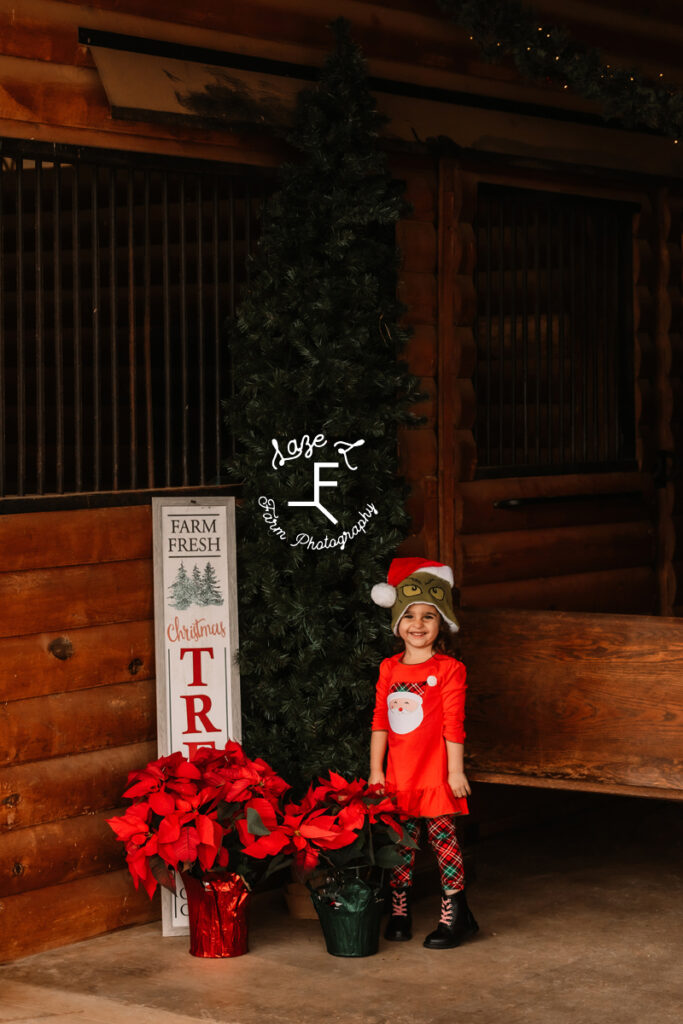 little girl wearing Grinch hat standing at Christmas tree