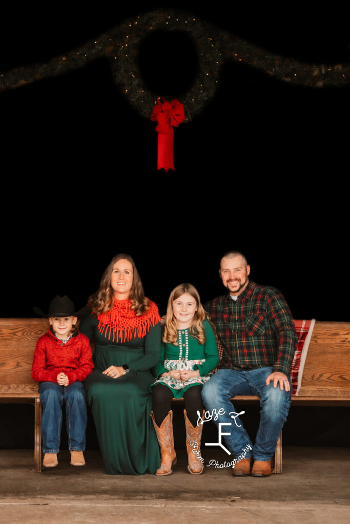 Family of 4 sitting on pew under Christmas Wreath