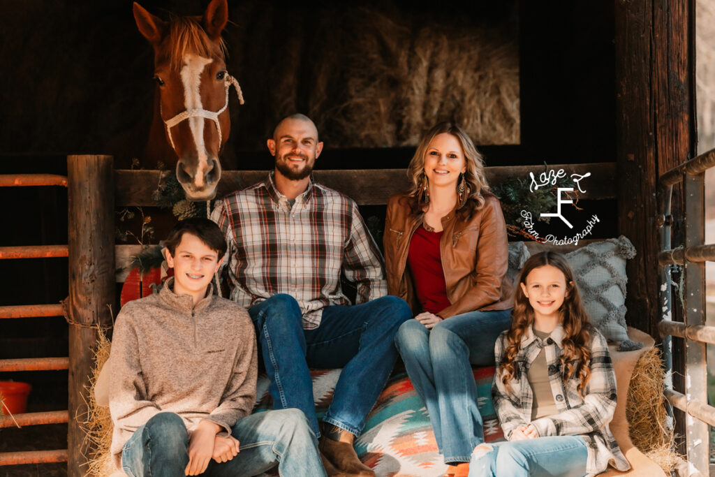 Family of 4 sitting with Gus in the barn