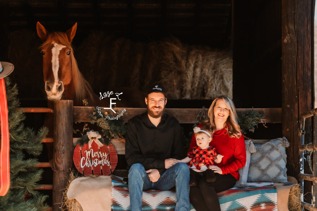 Mom and Dad with baby girl sitting in the barn with Gus