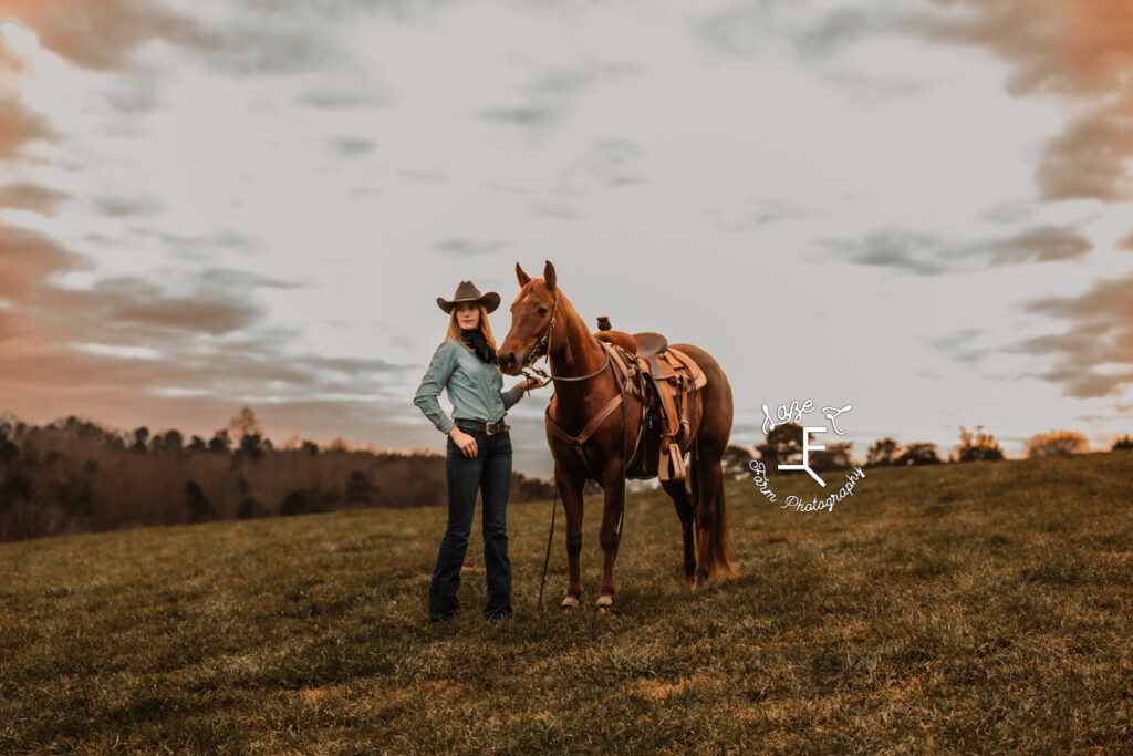 cowgirl standing on a hill with her horse