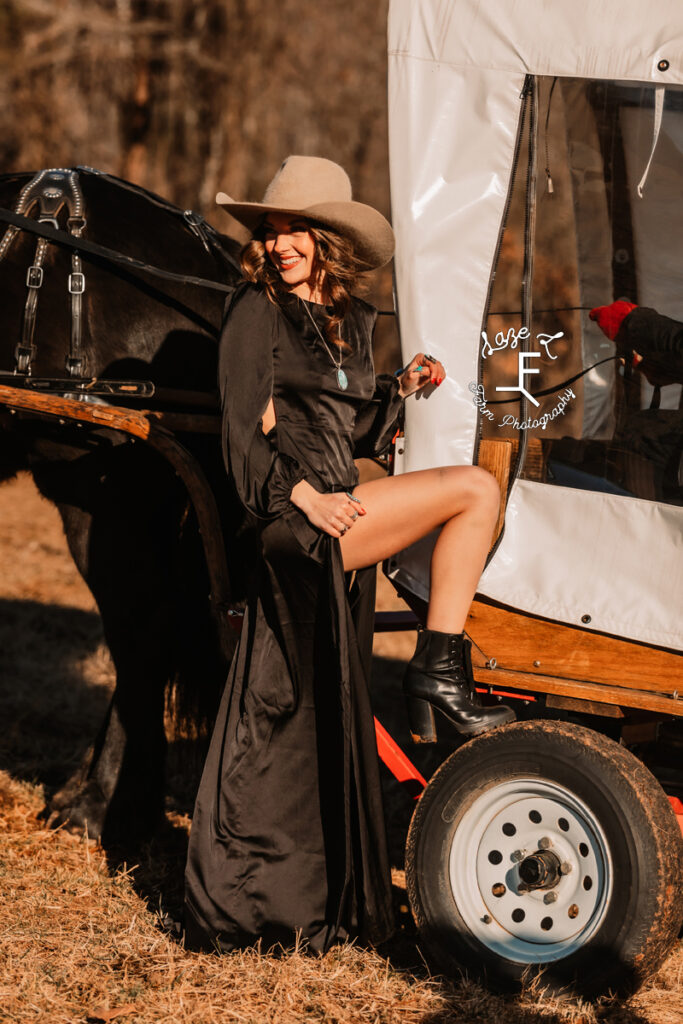 Model wearing black silk dress in front of covered wagon