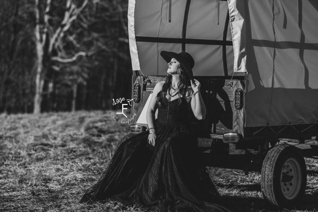 model in long black dress sitting on covered wagon step in black and white