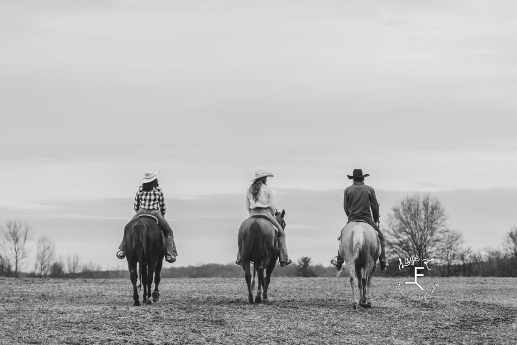 2 cowgirls and a cowboy riding away in black and white