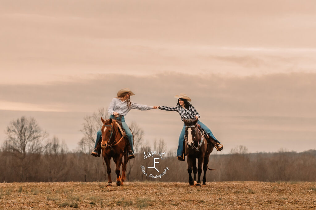 2 cowgirl best friends holding hands on horse back