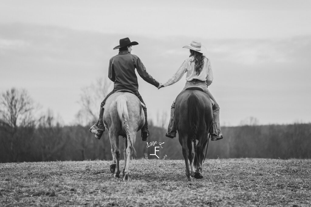 cowboy and cowgirl holding hands riding away in black and white